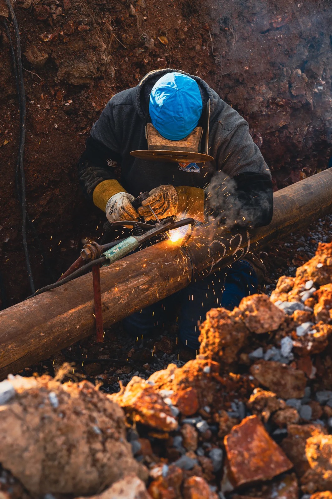 Welder working on a pipe in a trench with sparks flying